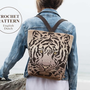 Op de afbeelding: Een gehaakte tijgerrugzak met bruine banden. De rugzak wordt gedragen door een persoon die op een houten oppervlak staat.