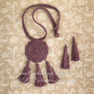 May include: A set of crocheted jewelry in a mauve color. The set includes a necklace with a round pendant and three tassels, and a pair of earrings with tassels.