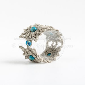 May include: A crocheted bracelet with a beige background and blue gemstone accents. The bracelet is made with a delicate, intricate pattern and features a clear plastic insert.