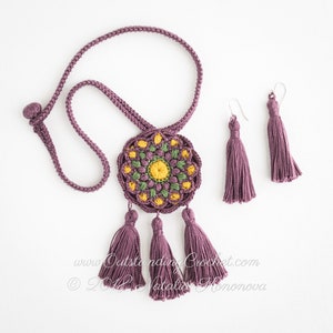 May include: A purple crocheted necklace with a round mandala pendant featuring green, yellow, and brown accents. The necklace has three purple tassels hanging from the pendant. The image also shows a pair of matching purple tassel earrings.
