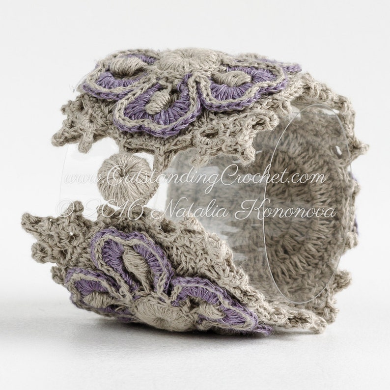 May include: A crocheted bracelet with a floral design in shades of beige and purple. The bracelet is made with a delicate stitch and features a raised flower pattern. The text "www.OutstandingCrochet.com &copy;2016 Natalia Hononova" is visible on the bracelet.