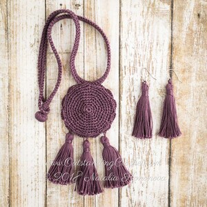May include: A set of crocheted jewelry in a deep purple color. The necklace features a round pendant with a tassel detail. The earrings are also tassel style.