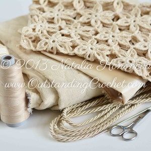 May include: A close-up of a beige crochet doily, a spool of beige thread, a ball of beige yarn, and a pair of silver scissors. The doily is made with a delicate flower pattern. The text "&copy; 2013 Natalia Komonowa www.OutstandingCrochet.com" is visible on the fabric.