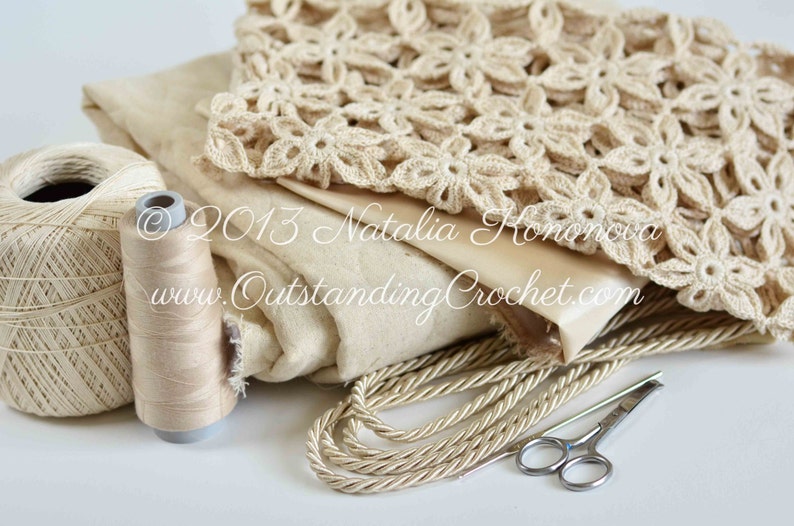 May include: A close-up of a beige crochet doily, a spool of beige thread, a ball of beige yarn, and a pair of silver scissors. The doily is made with a delicate flower pattern. The text "&copy; 2013 Natalia Komonowa www.OutstandingCrochet.com" is visible on the fabric.