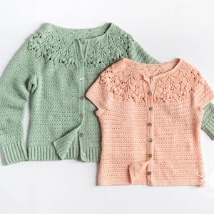 May include: A sage green long-sleeve crochet cardigan and a peach short-sleeve crochet cardigan, both featuring a round yoke with a textured leaf and bobble stitch pattern, a button-down front with small buttons, and ribbed cuffs and hems.