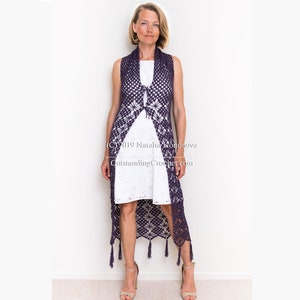 Può includere: Un lungo gilet all'uncinetto con un motivo geometrico e frange. Il gilet è viola e viene indossato sopra un vestito bianco.