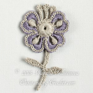 May include: A crocheted flower in a purple and beige colour scheme. The flower has five petals and a centre with a small hole. The flower is attached to a stem with two leaves.
