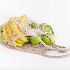 Könnte beinhalten: Eine beige gehäkelte Netztasche gefüllt mit grünen Äpfeln und gelben Bananen. Die Tasche hat einen langen Henkel.