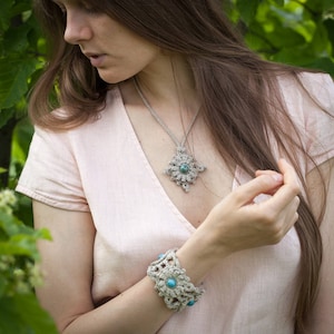 Puede incluir: Una mujer lleva una blusa de crochet rosa claro con un collar y una pulsera de crochet con piedras turquesa. El collar tiene un colgante en forma de estrella.