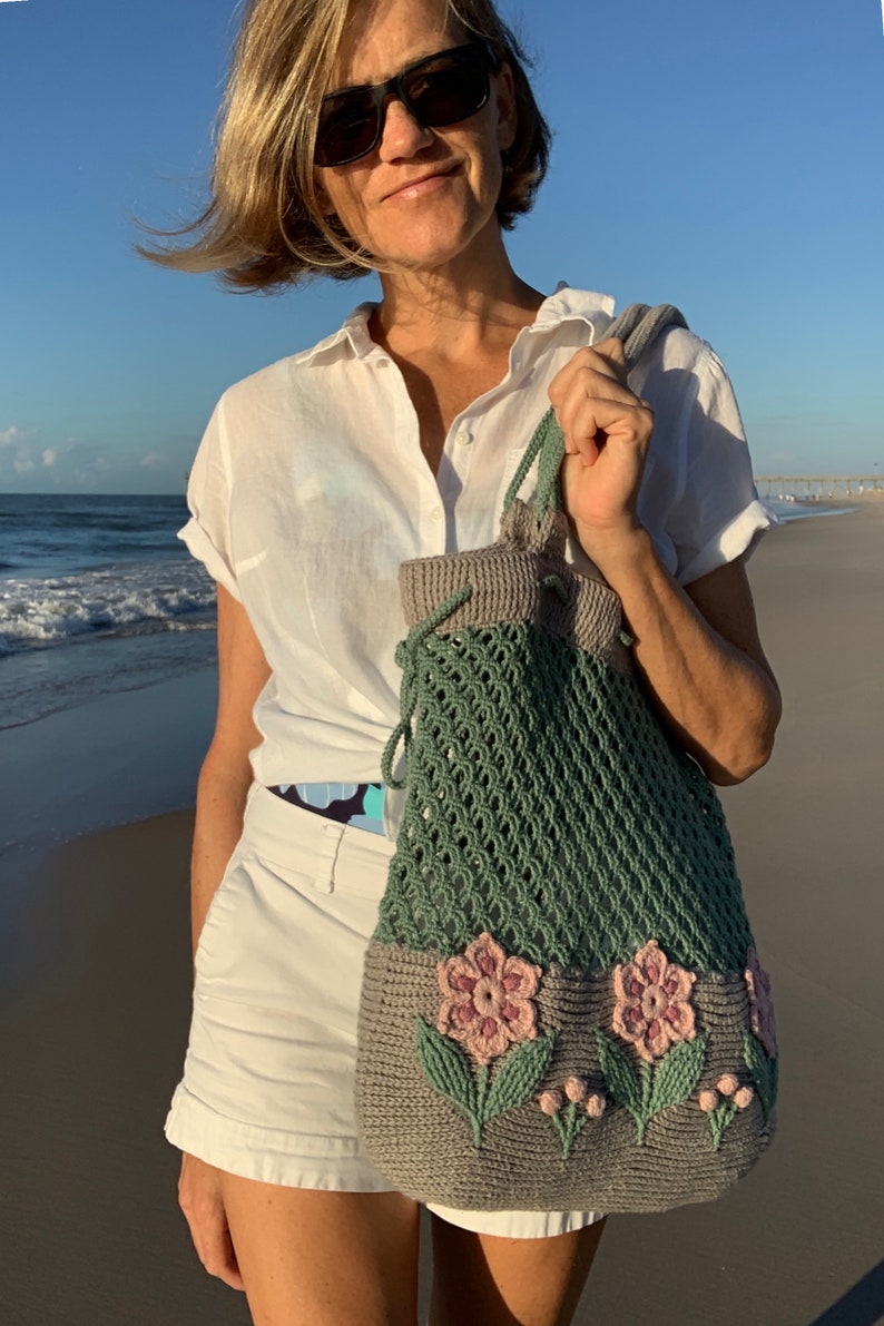 Crochet bag pattern: a shoulder bag with a combination of embossed crochet bottom with 3D flowers and leaves and a net top. Beautiful original multi-corded handles and a drawstring that goes through the top.