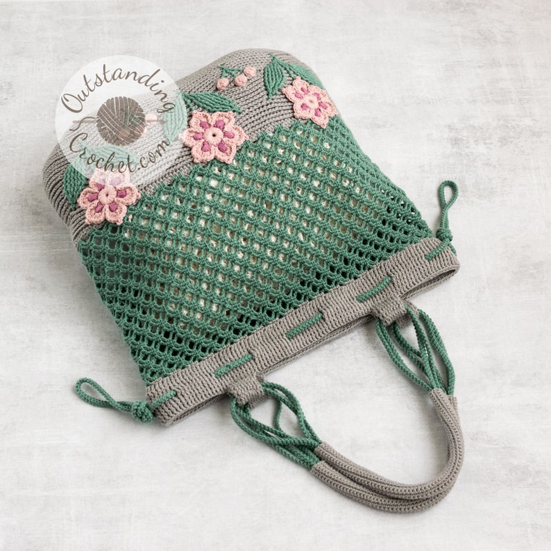 Crochet bag pattern: a shoulder bag with a combination of embossed crochet bottom with 3D flowers and leaves and a net top. Beautiful original multi-corded handles and a drawstring that goes through the top.