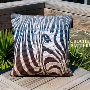 May include: A crocheted zebra cushion with a brown, white and blue ombre design. The cushion is sitting on a wooden bench. CROCHET PATTERN English Dutch.