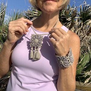 May include: A woman wearing a light purple sleeveless top with a crocheted necklace and bracelet. The necklace has a large, square pendant with a floral design and tassels. The bracelet is a wide band with a similar floral design.