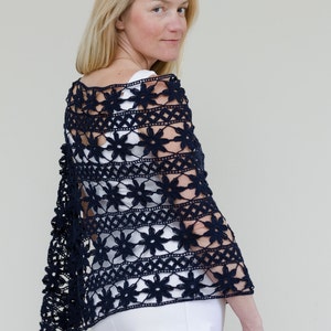 Peut inclure: Un châle en crochet bleu marine avec un motif floral. Le design ajouré présente des motifs floraux et des formes géométriques répétées. Le châle est porté sur un haut blanc et est un article fait à la main.