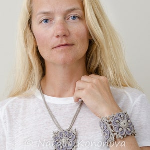 May include: A woman wearing a white t-shirt with a crocheted necklace and bracelet. The necklace and bracelet are made of beige and purple yarn and feature a floral design. The text "&copy; Natalia Konovova Outstanding Crochet.com" is visible on the t-shirt.