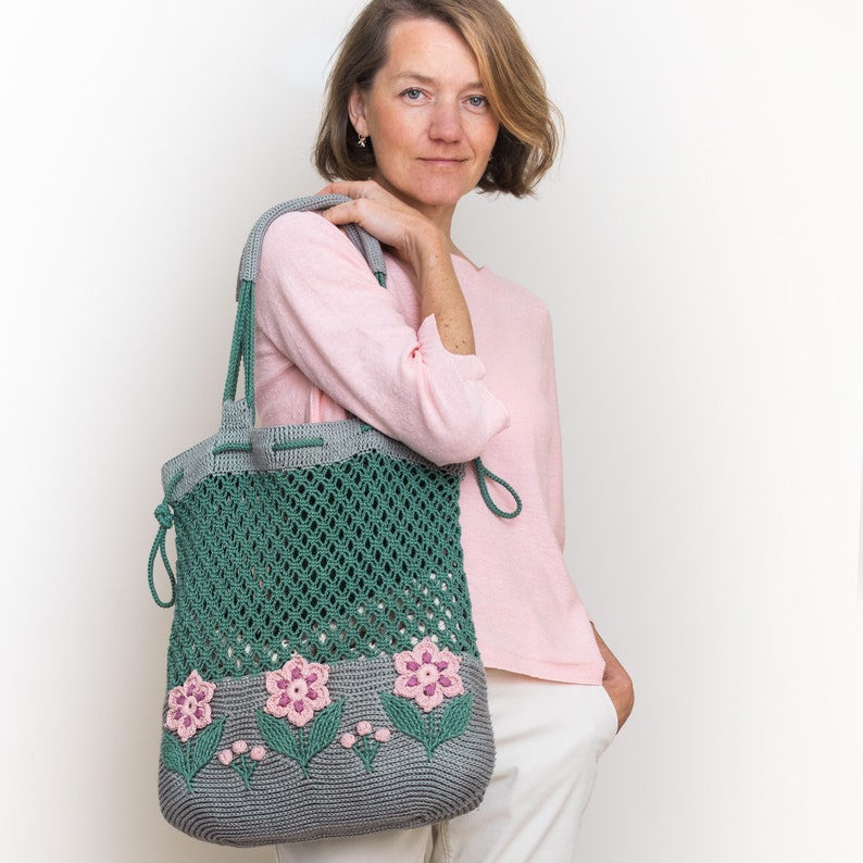 Crochet bag pattern: a shoulder bag with a combination of embossed crochet bottom with 3D flowers and leaves and a net top. Beautiful original multi-corded handles and a drawstring that goes through the top.