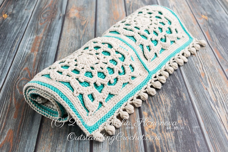 Puede incluir: Una alfombra de crochet con un dise&ntilde;o blanco y turquesa. La alfombra est&aacute; enrollada y tiene flecos en los bordes. La alfombra est&aacute; sobre una superficie de madera. (c) 2018 Natalia Konova OutstandingCrochet.com