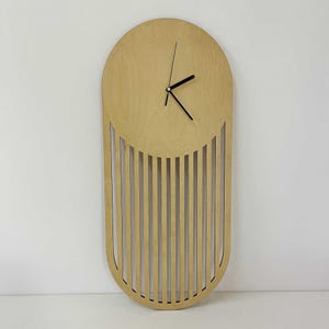 Pode incluir: Um relógio de parede de madeira clara. O relógio tem um design único, com uma parte superior arredondada e ripas verticais na parte inferior. Os ponteiros do relógio são pretos. Este relógio decorativo é adequado para uma casa moderna. Medidas em centímetros.