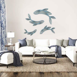 Peut inclure: Quatre pièces d'art mural représentant des baleines bleues avec un design linéaire sont exposées sur un mur blanc. Les baleines sont de tailles différentes et disposées dans une composition dynamique. La pièce comprend un canapé blanc, des coussins et une table basse ronde.