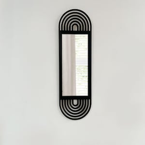 May include: A black, elongated wall mirror with a rectangular central mirror and a decorative arched design at the top and bottom. The arched design features concentric semi-circles. The mirror is mounted on a white wall.