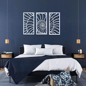 May include: Three white, abstract wall art panels with a nautilus shell design hang above a bed with white bedding and a navy blue blanket. The bedroom has a dark blue wall, two nightstands, and pendant lights.
