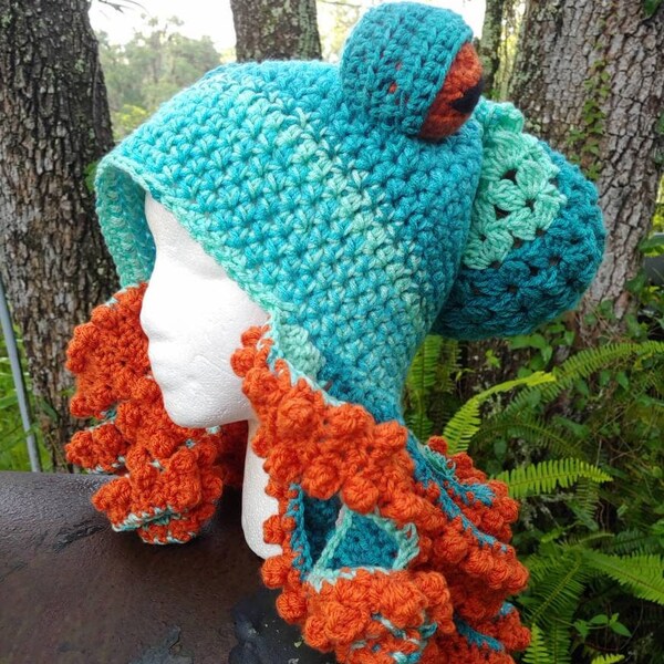 May include: A crocheted octopus hat with a teal and green body and orange tentacles. The hat has a hood and is made with a textured stitch.