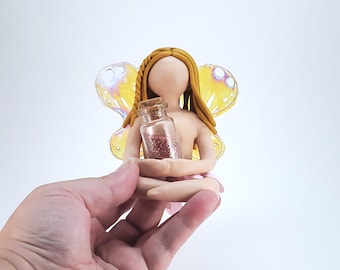 May include: A small fairy figurine with yellow hair and wings, holding a glass bottle filled with pink glitter.