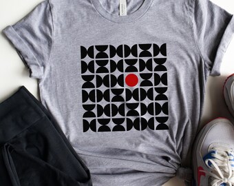 May include: A gray t-shirt with a black and red geometric design. The design features a pattern of black semi-circles and a single red circle. Black leggings and white sneakers with blue accents are also in the image.