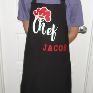 May include: A black chef's apron with a red chef's hat and the text "Chef Jacob" in white and red lettering.