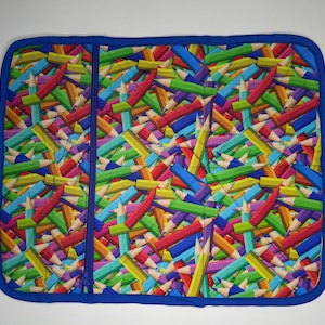 May include: A blue fabric hot pad with a zipper closure. The fabric has a colorful pattern of many colored pencils.