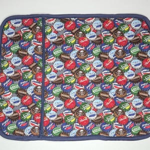 May include: A blue pot holder with a pattern of colorful bottle caps. The bottle caps have various designs, including "Pop", "Soda", "Thirsty", and a skull and crossbones.