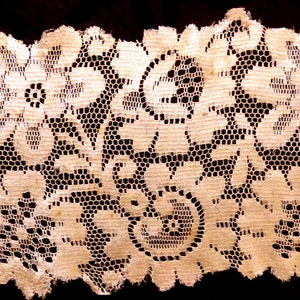 May include: A close-up of a delicate white lace trim with a floral pattern. The lace is made of a fine mesh fabric with intricate details.