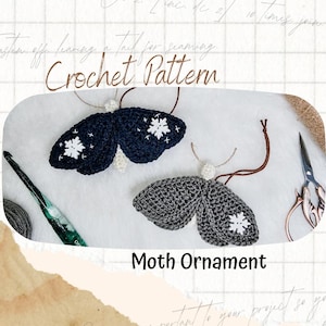 Op de afbeelding: Twee handgemaakte gehaakte mot-ornamenten, één in donker marineblauw en één in antracietgrijs, beide met witte geborduurde sneeuwvlokdetails op de vleugels. De tekst Crochet Pattern en Moth Ornament is zichtbaar op de afbeelding.