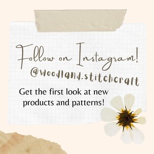 May include: A white piece of paper with a grid pattern, taped to a beige background. The paper has handwritten text that says "Follow on Instagram! @woodland.stitchcraft Get the first look at new products and patterns!" A white flower with a brown center is in the bottom right corner of the paper.