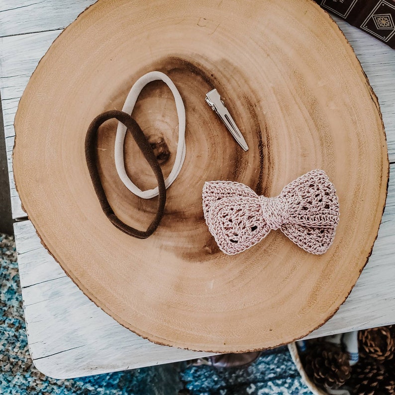 May include: Two brown and white hair ties and a pink crocheted bow on a wooden surface.