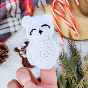 May include: A white crocheted bear finger puppet featuring a rounded head with small ears, a snout, and black embroidered eyes and nose. The bear has a circular body and is crafted from white yarn with a visible textured stitch pattern throughout.