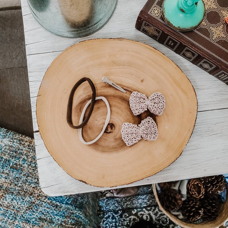 May include: Two small pink crocheted bows with a silver hair clip and two brown and white hair elastics on a wooden surface.