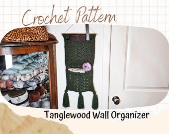 May include: A green crocheted wall organizer with tassels hanging from the bottom. The organizer has two pockets and is labeled "Tanglewood Wall Organizer".
