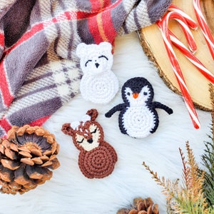 May include: Three small crochet appliques featuring a white polar bear, a black and white penguin, and a brown deer with white spots. Each figure is crafted with yarn and displays a distinct animal face with embroidered details.
