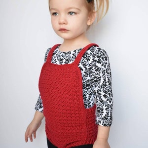 May include: A young child wearing a red crocheted overall with black leggings and a black and white patterned shirt.