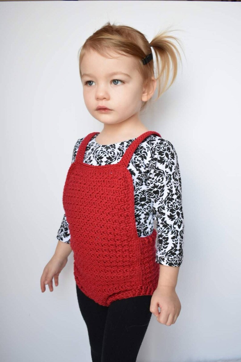 May include: A young child wearing a red crocheted overall with black leggings and a black and white patterned shirt.
