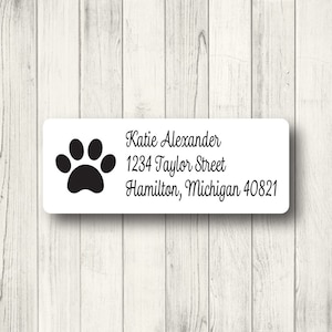 May include: White rectangular label with a black paw print and the text "Katie Alexander, 1234 Taylor Street, Hamilton, Michigan 40821". The label is set against a light wood grain background.