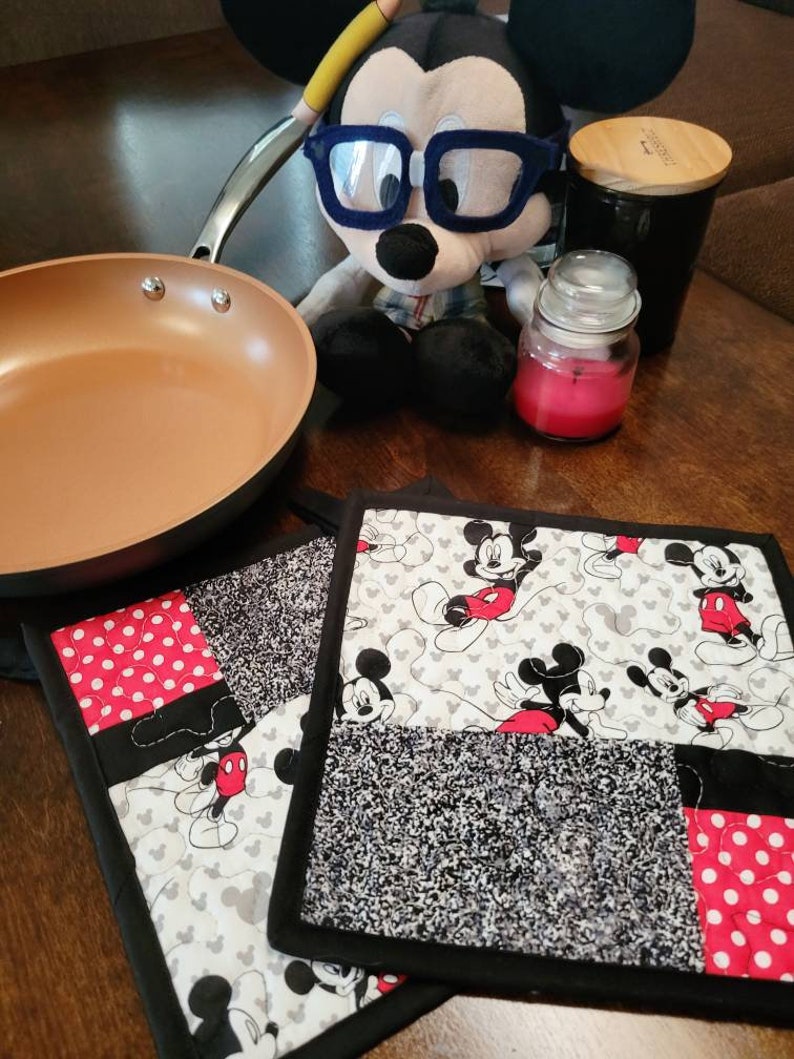 May include: Two black and white Mickey Mouse themed pot holders with red accents. One pot holder has a black and white polka dot pattern and the other has a black and white Mickey Mouse print.