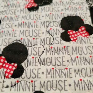 May include: White fabric with black and red polka dot Minnie Mouse heads. The fabric is printed with the words "Minnie Mouse" repeatedly.