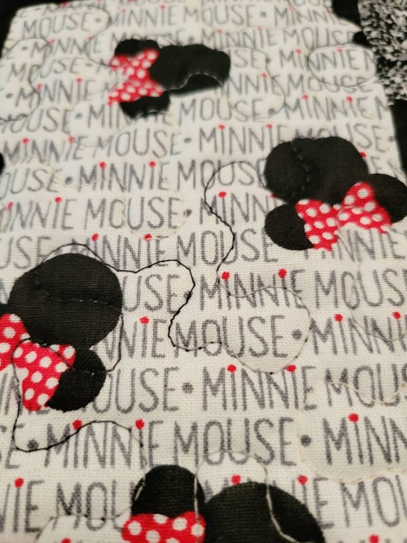 May include: White fabric with black and red polka dot Minnie Mouse heads. The fabric is printed with the words "Minnie Mouse" repeatedly.