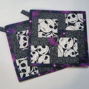 May include: Two black and white fabric pot holders with a purple border. The fabric features a repeating pattern of Jack Skellington's face from The Nightmare Before Christmas.