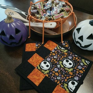 May include: Two black and orange quilted pot holders with a Jack Skellington pattern and the words "Master Fright" repeated on the fabric.