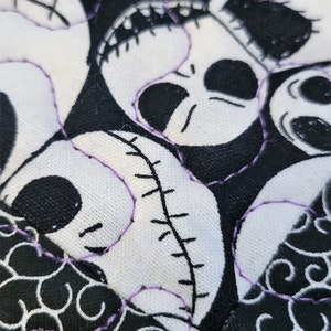 Puede incluir: Primer plano de una tela negra y blanca con un patr&oacute;n repetitivo de remolinos. La tela est&aacute; cosida con hilo morado. La tela presenta un dise&ntilde;o de patchwork con m&uacute;ltiples caras blancas con ojos negros y bocas cosidas.