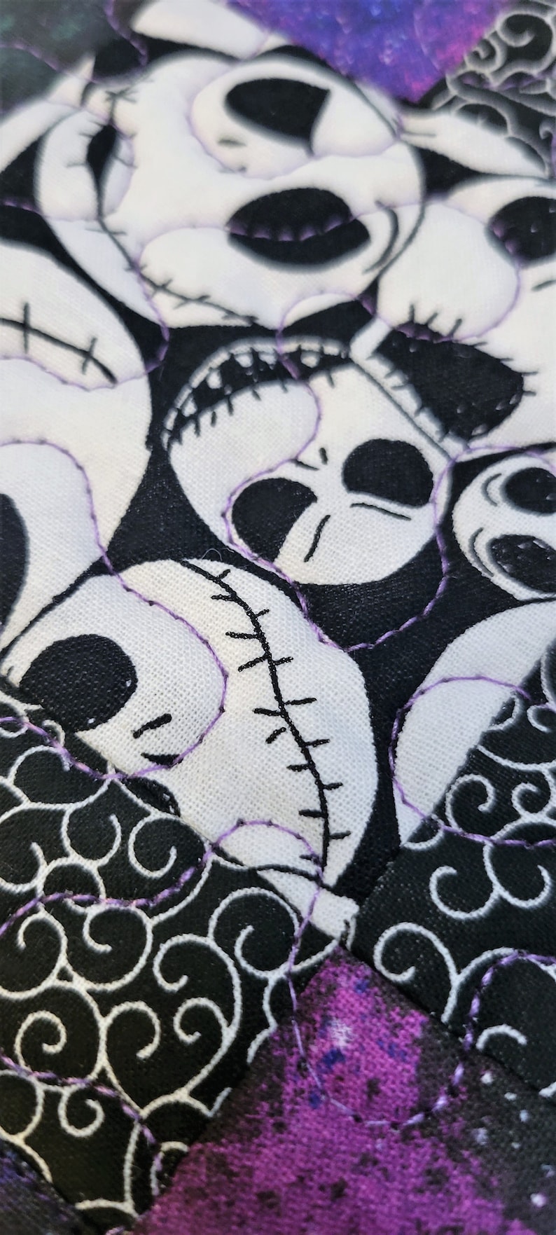 Puede incluir: Primer plano de una tela negra y blanca con un patr&oacute;n repetitivo de remolinos. La tela est&aacute; cosida con hilo morado. La tela presenta un dise&ntilde;o de patchwork con m&uacute;ltiples caras blancas con ojos negros y bocas cosidas.