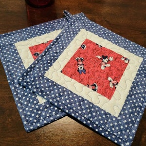 May include: Two blue and white polka dot fabric pot holders with a red and white fabric square in the centre featuring a Mickey Mouse print.